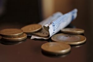 Sobre uma mesa uma nota de dinheiro de cor azul e algumas moedas espalhadas. Imagem ilustrativa texto abrir meu proprio negocio com pouco dinheiro.