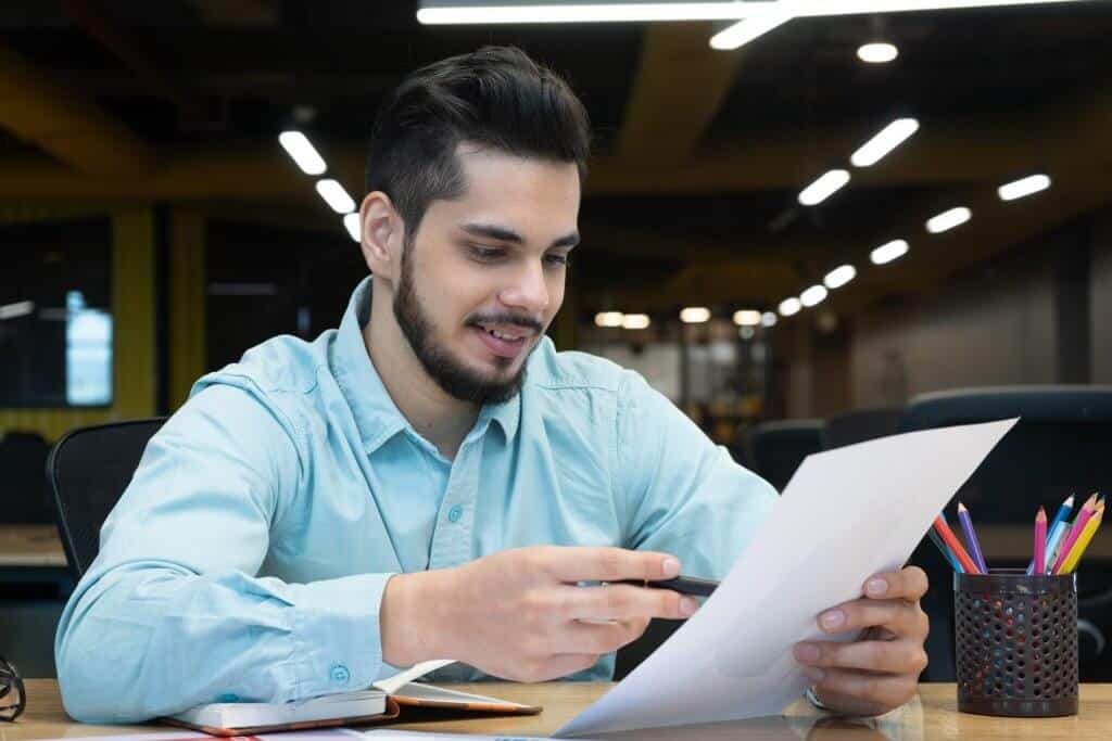 Homem sorrindo e usando camisa azul, segurando papel em escritório. Ilustração do texto sobre franqueado máster.