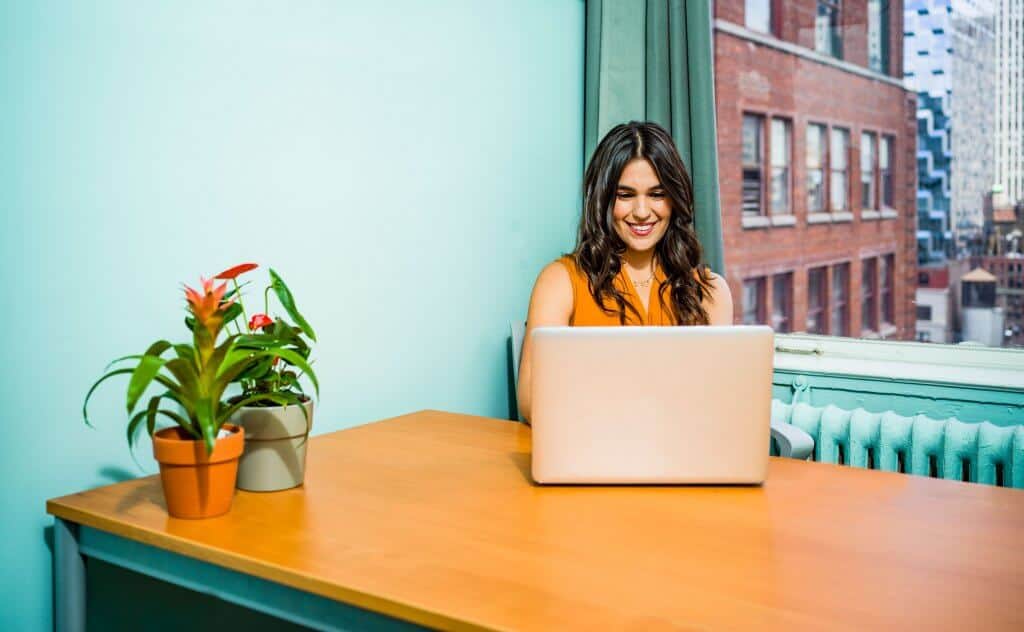 mulher de blusa laranjada sorrindo em frente a computador em mesa de madeira ilustração de franquia de negócios e serviços
