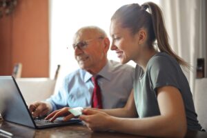 Homem mais velho usando uma camisa social e uma gravata vermelha ao lado de uma mulher. Ambos estão sentados e olhando para um computador. Imagem ilustrativa do texto sobre franquias baratas e lucrativas 2023.