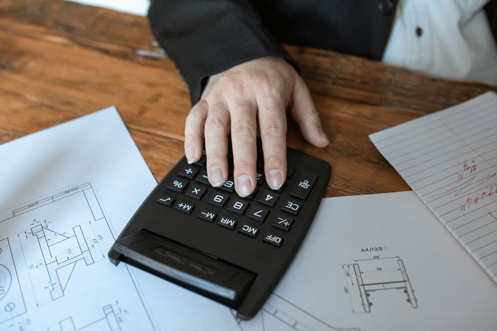Mão sobre uma calculadora em cima de uma mesa cheia de papéis. Imagem ilustrativa do texto franquias de baixo custo para investir.
