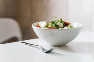 uma vasilha branca com salada com uma colher do lado. Imagem ilustrativa do texto sobre franquias segmento alimentação