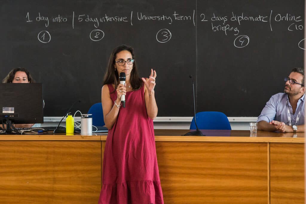 mulher de vestido longo cor de rosa falando em microfone em sala de aula. Imagem ilustrativa texto franquias segmento serviços educacionais