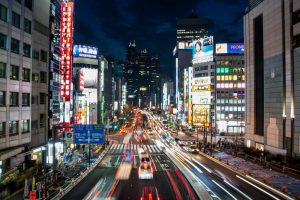 Cidade oriental com ruas iluminadas por faróis de carros nas cores vermelho e branco. Ilustração do texto sobre abrir franquia no Japão.