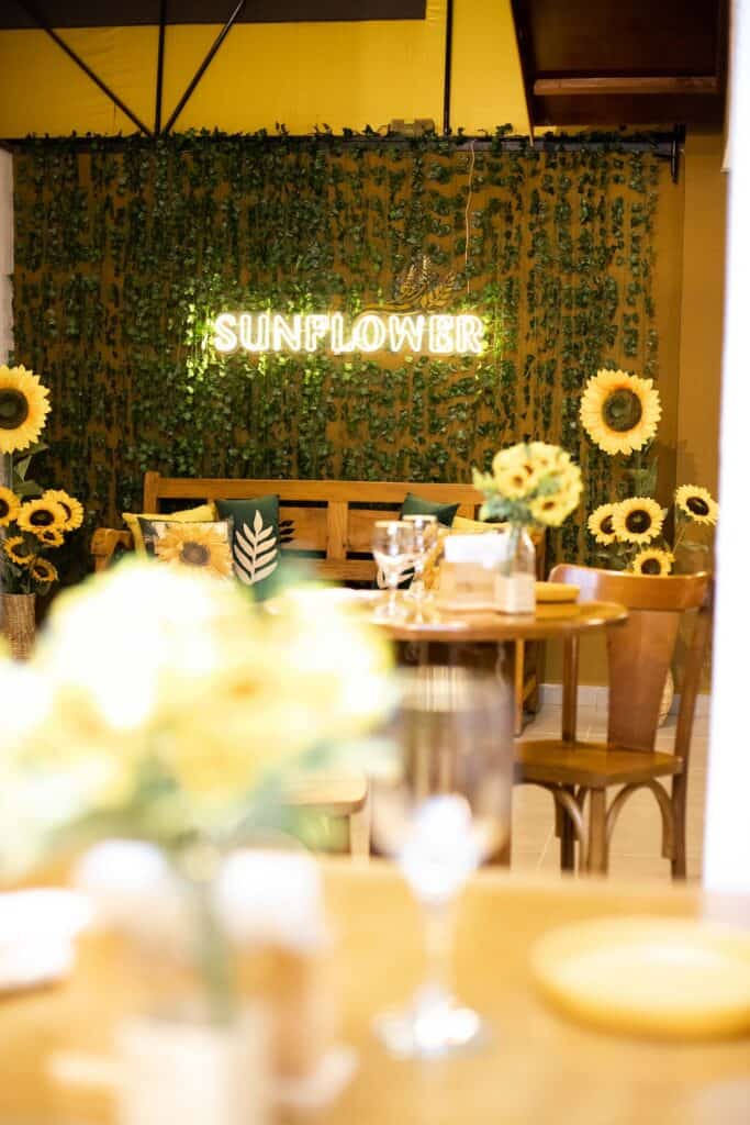 Mesas no restaurante Sunflower e girassóis ao fundo.